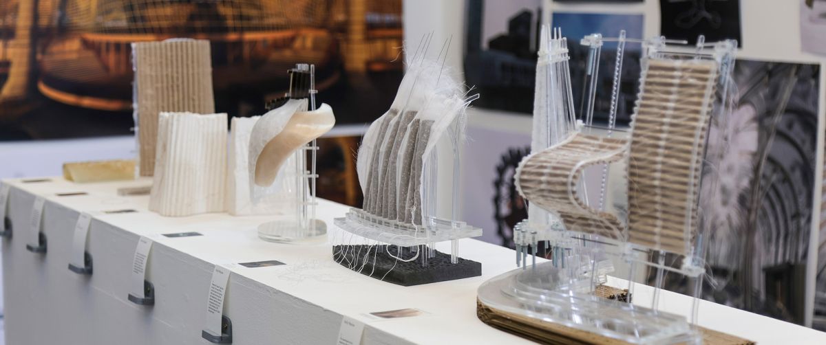 End of Year Exhibition showing a Masters Design Studio. The image displays architectural models made from various materials like cardboard, fabric, and clear plastic.