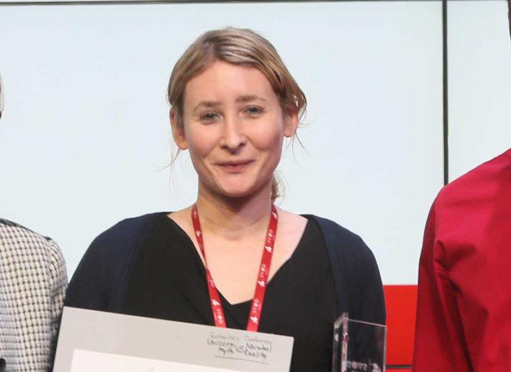 Blond woman wearing black top, red lanyard and holding paper folder