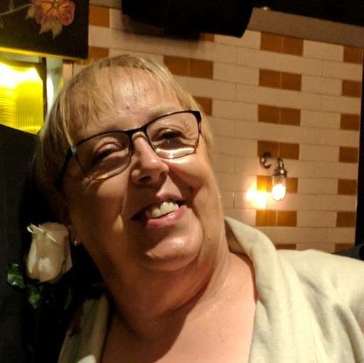 Ahead shot of a spectacled White woman in a cream top, short hair and smiling