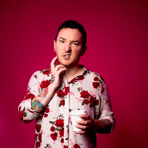 Chris is wearing a pink shirt with red flowers on, he is holding a coffee cup against a red background