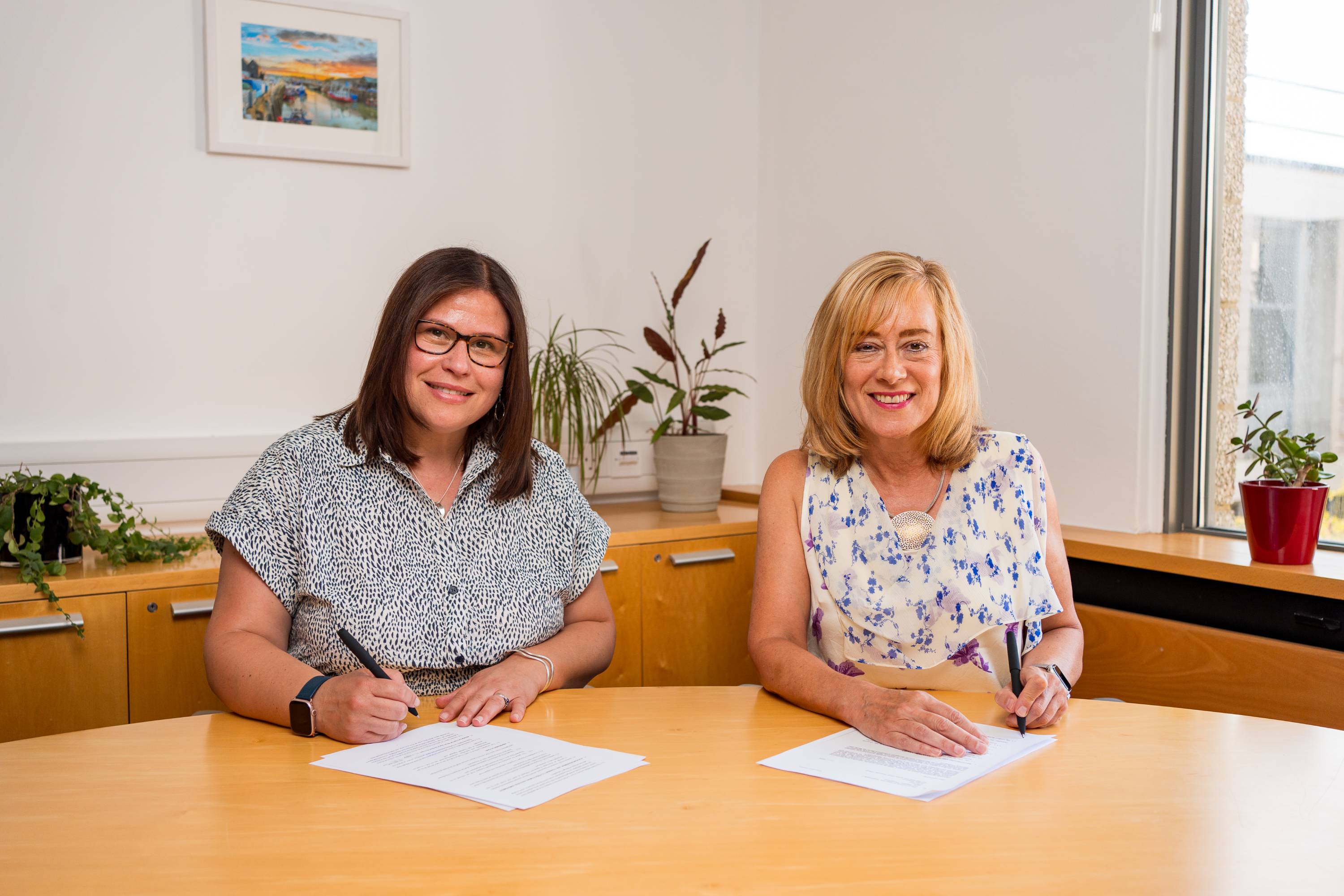 Prof Jane Harrington and Prof Georgina Randsley de Moura smile as they sit to sign contracts