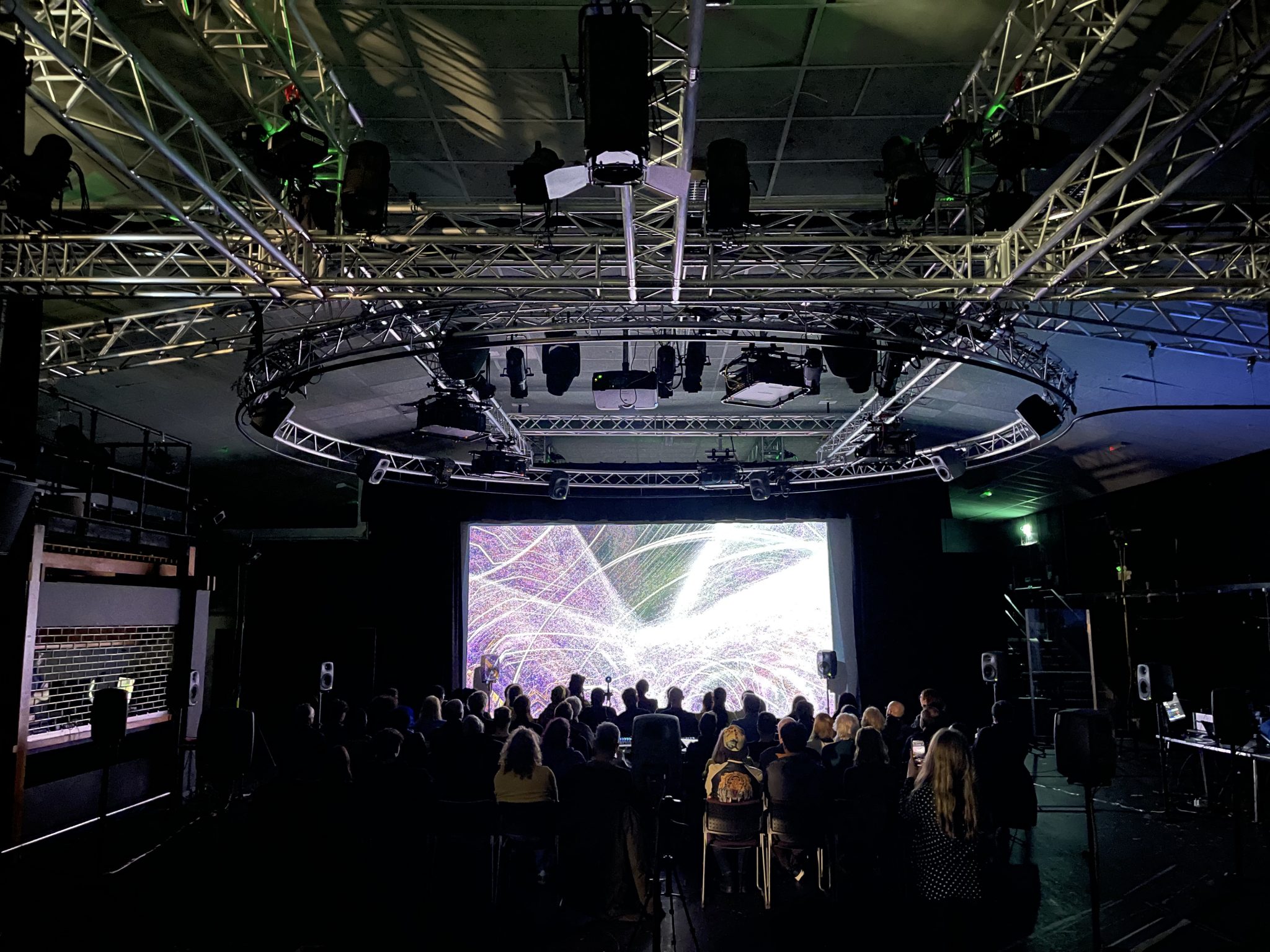A crowd stands in front of a large screen with an abstract visualisation