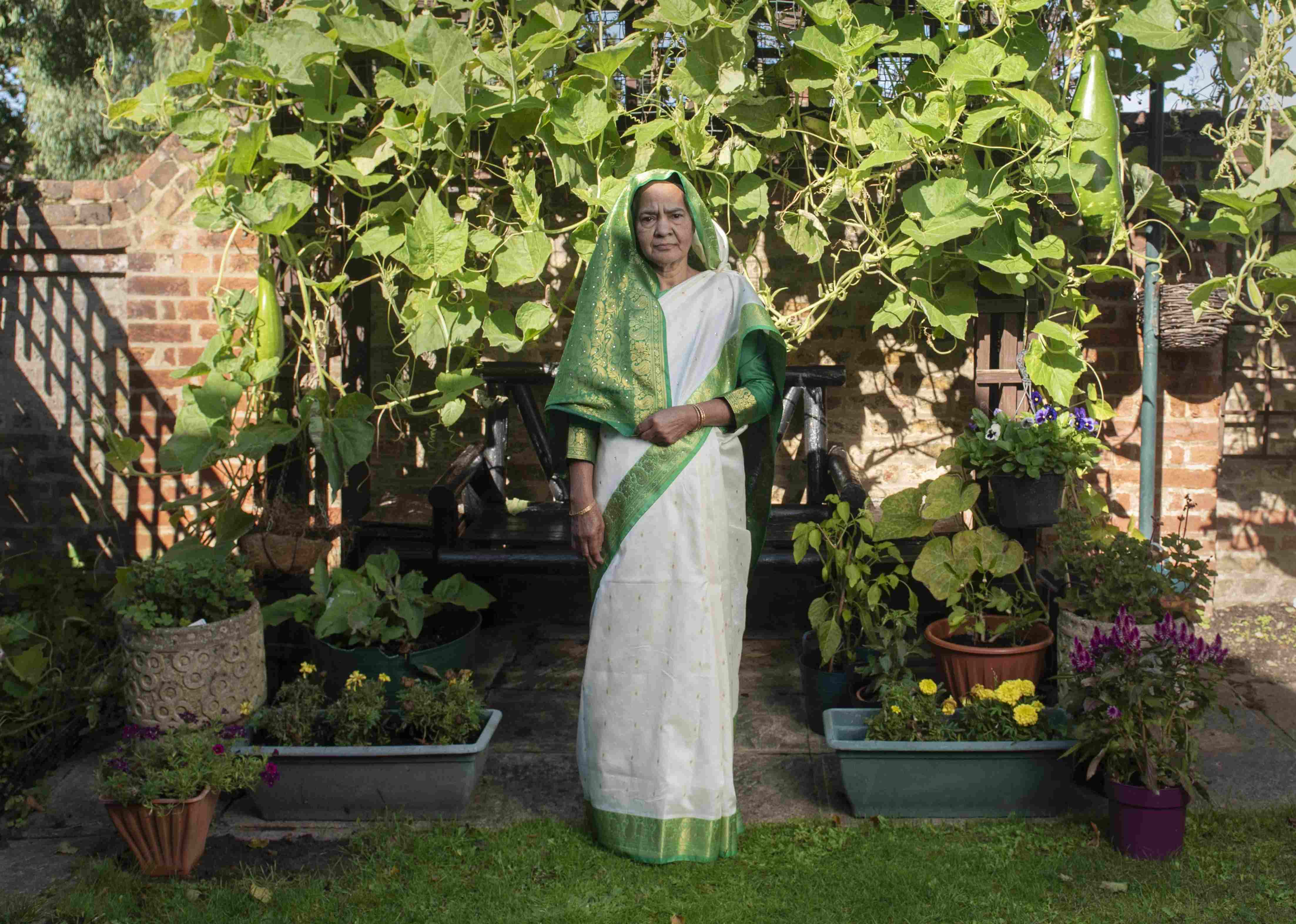 South Asian female in white and green saree stands in a garden