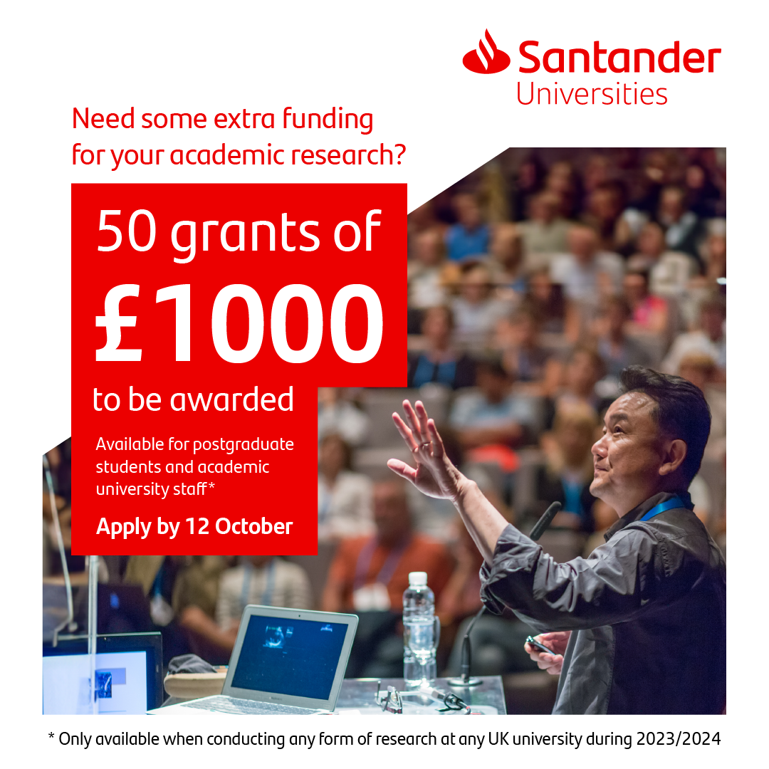 Lecturer pointing at a screen and room full of students. Laptop on the table and a bottle of water