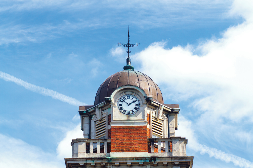 A photo showing the top of the pembroke building with the clock tower with a background a blue sky with clouds.