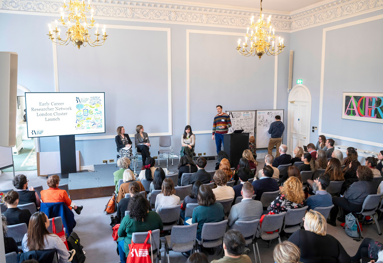 People at the British Academy Early Careers Network event launch, seated and listening to a presenter on stage.