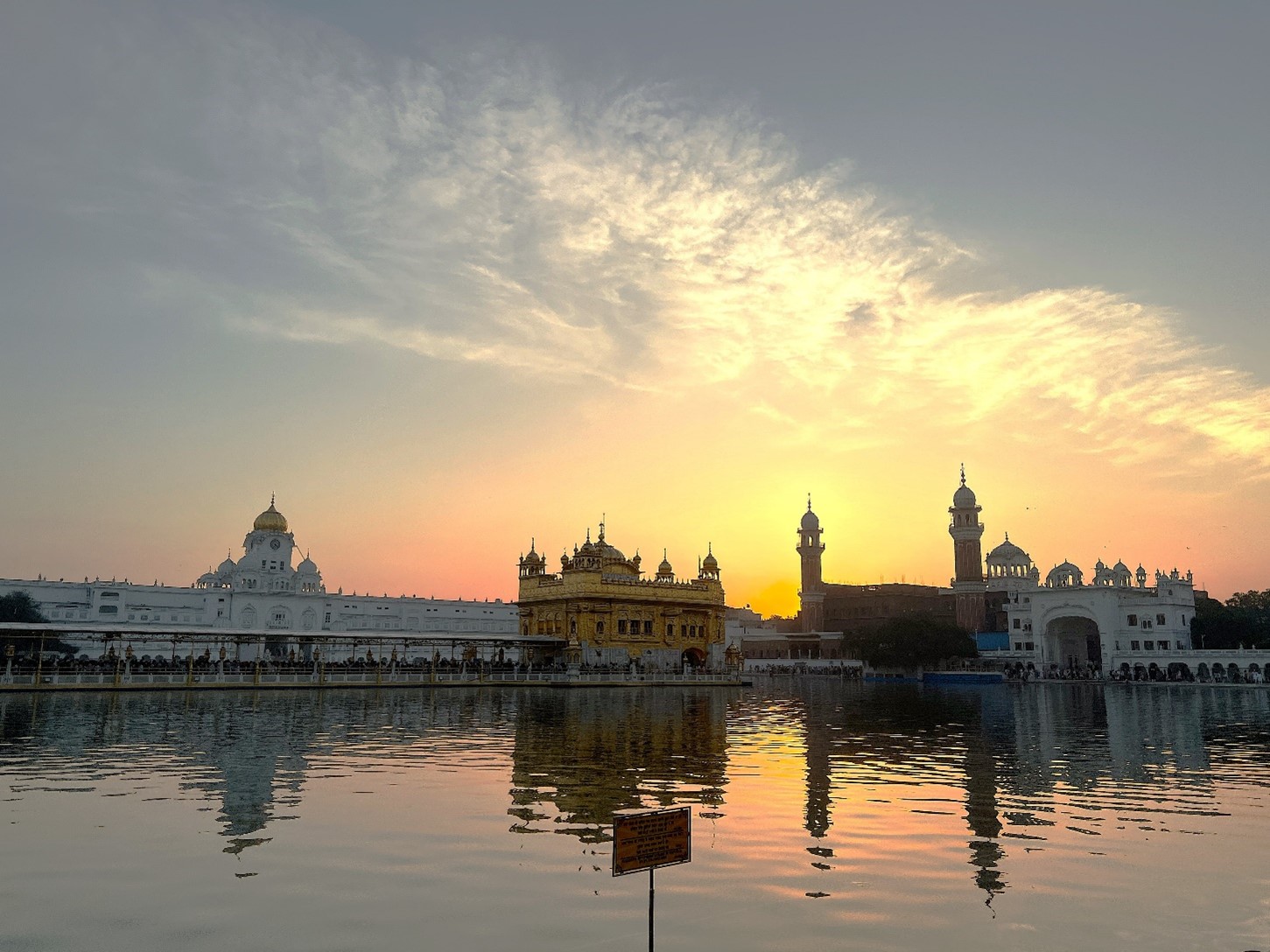 a temple that sits beside the water and has several towers, there are clouds in the background red from the sun