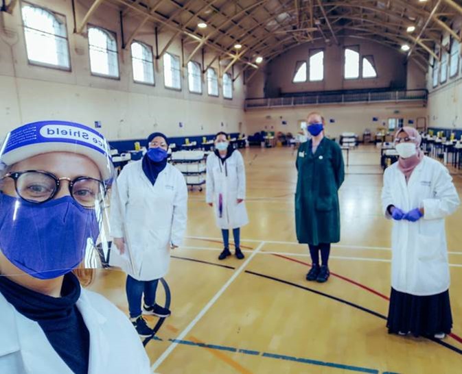 Close up of five people wearing lab coats, masks and safety glasses inside indoor sports hall laboratory