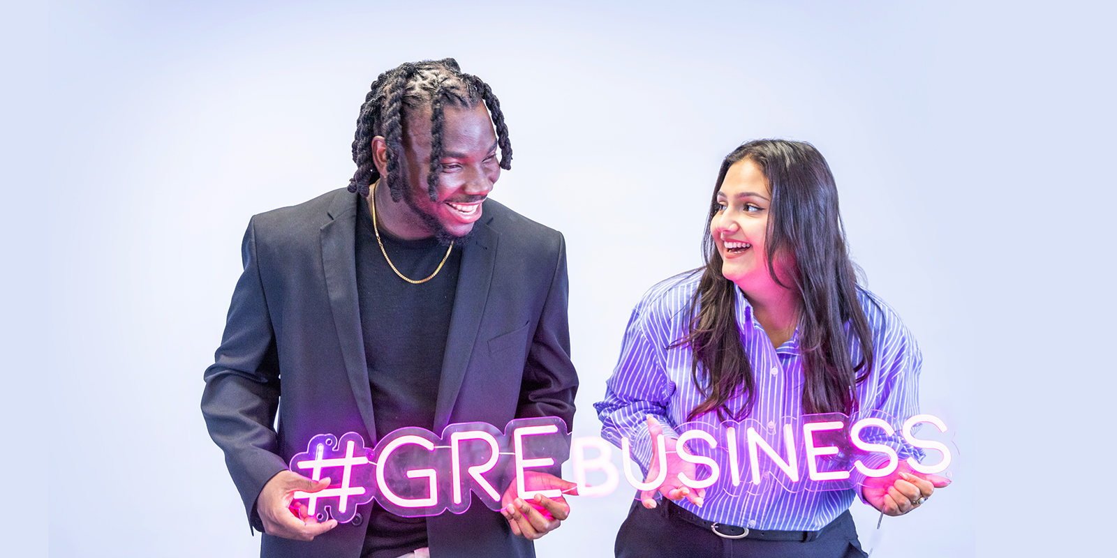 A man and a women standing holding a pink neon sign which says '#GreBusiness