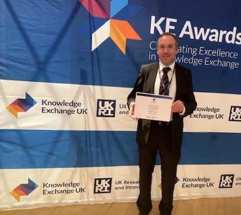 A suited man holds a certificate 